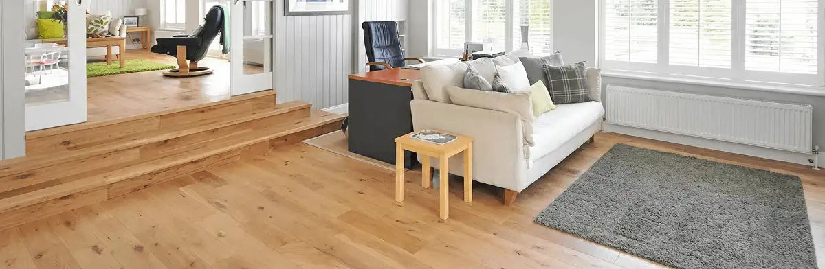 A modern living room with professionally installed laminate flooring, a beige sofa, a small side table, a gray rug, and large windows with white shutters in Stamford, CT